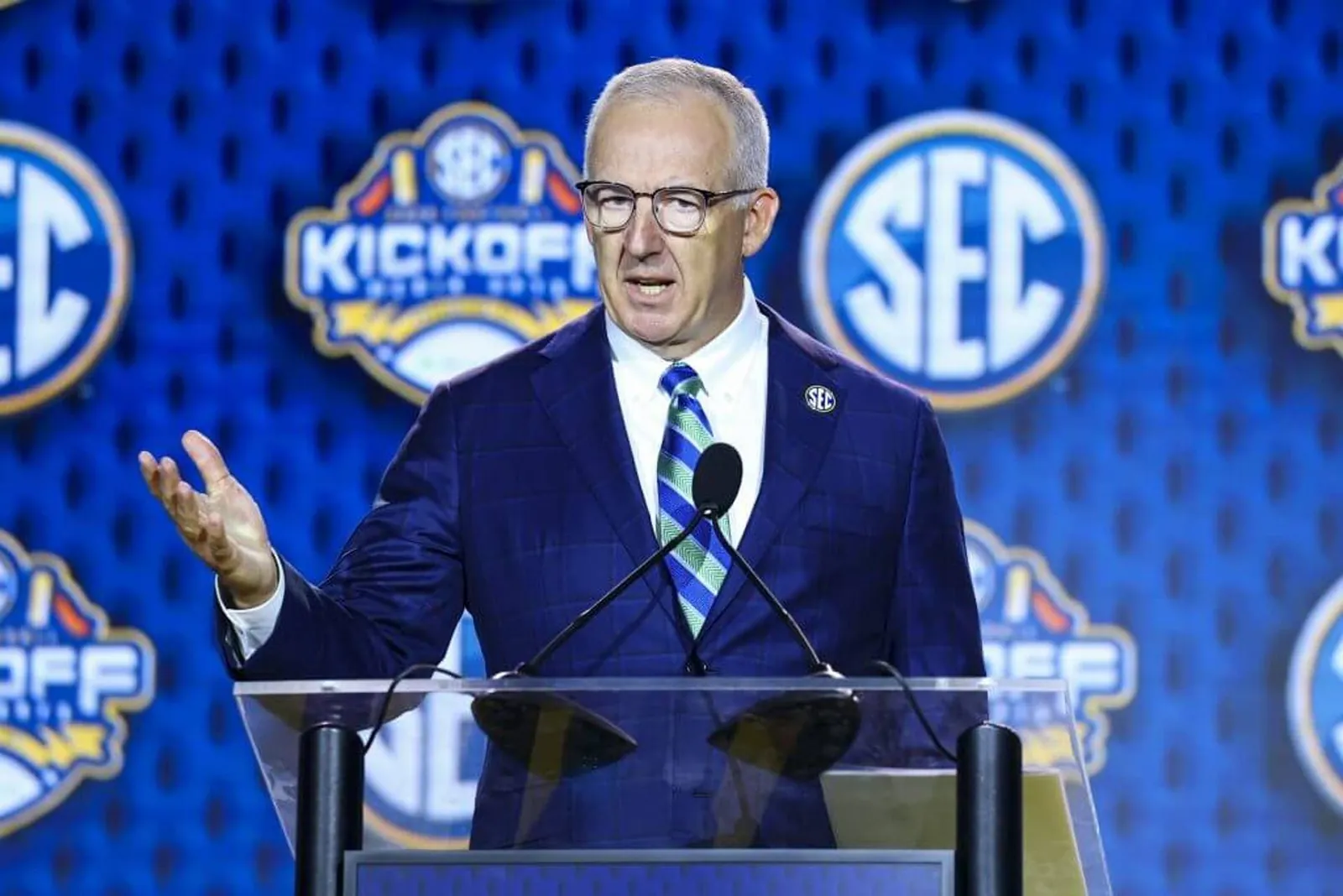 Greg Sankey speaks behind a microphone and in front of a backdrop of SEC logos